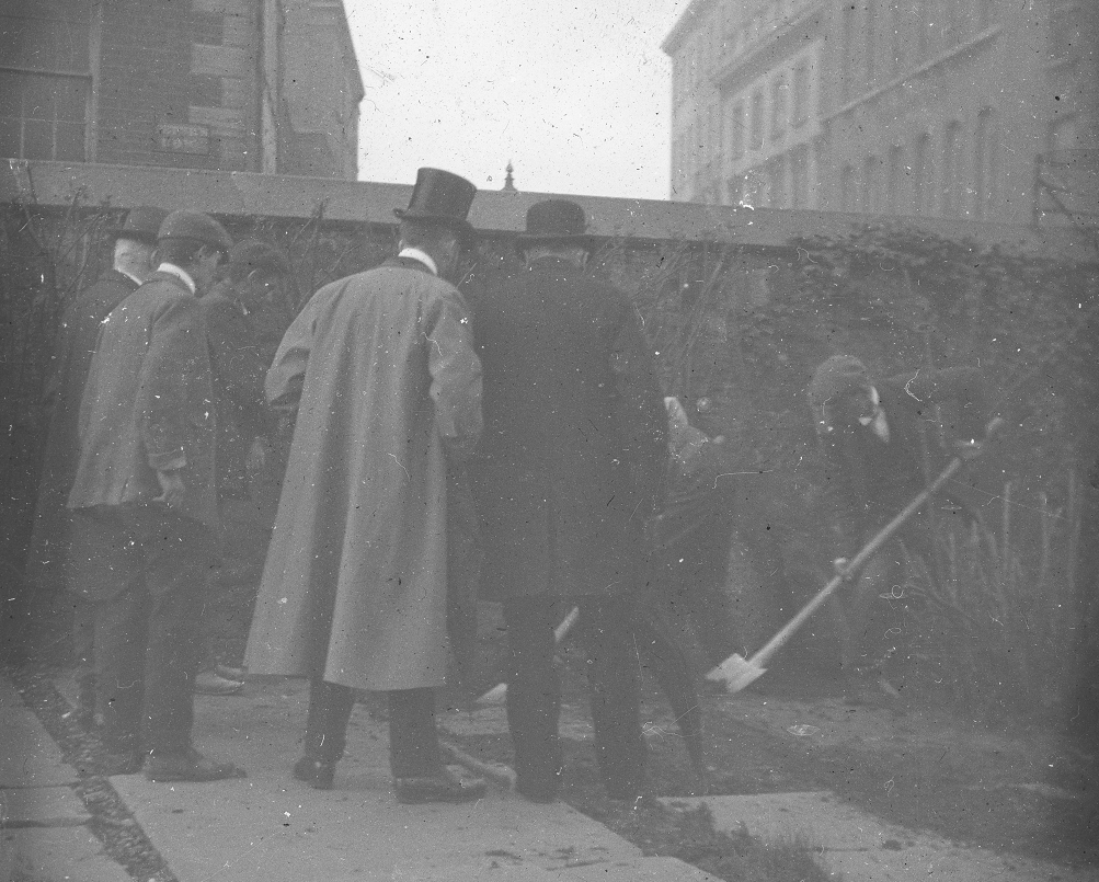 Excavation being conducted at the west wall of the graveyard. In the background we see the buildings of the Adelaide Hospital on the north side of Peter Street.