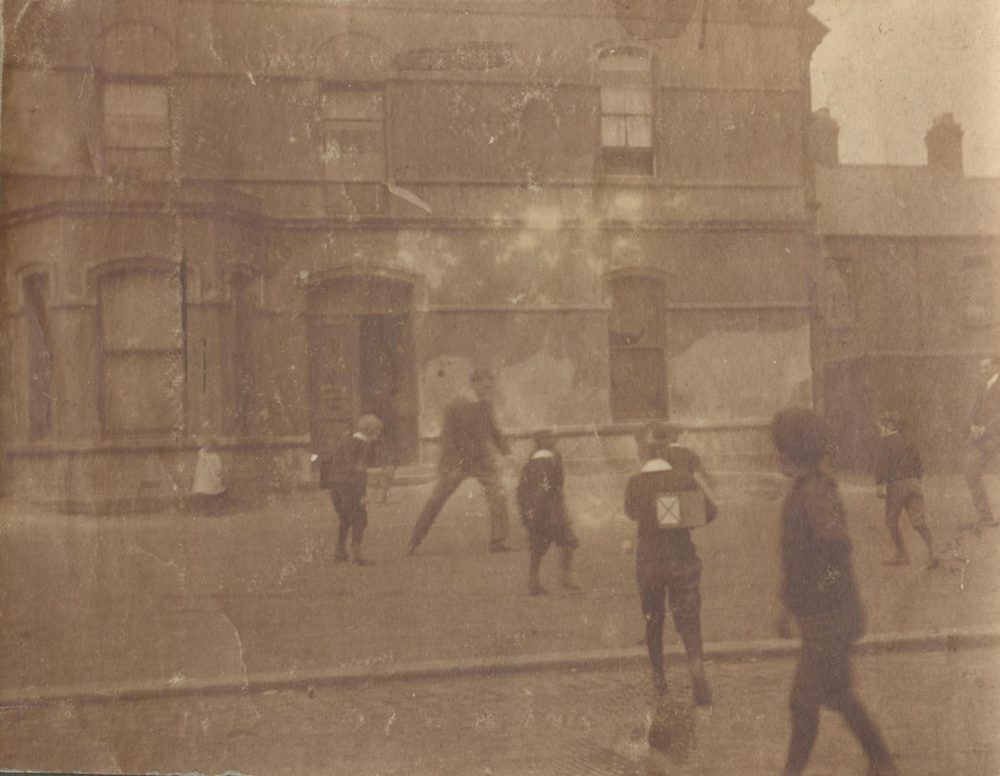 Image labelled &lsquo;H.G. Studdart Kennedy', which appears to show him kicking football with young people in front of the Mission building, RCB Library MS 295