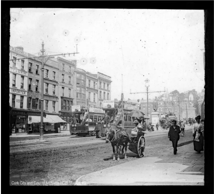 Figure 6: Lantern slide showing John Gilbert's store at 120 Patrick Street. Second building from the left, with sign reading 'Print Seller. Frame Maker. Celebrated for Spectacles. Gilberts. (Cork City Archive - PH/CM/127)
