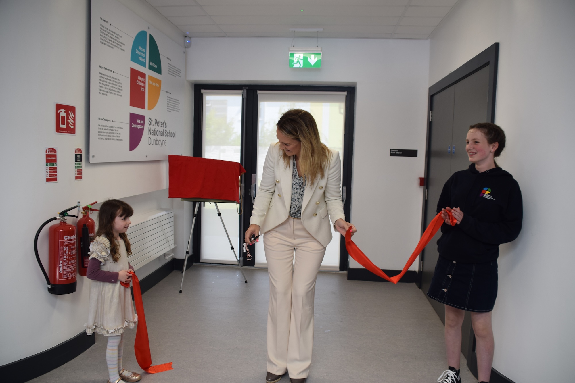Minister Helen McEntee, assisted by two pupils, cuts the ribbon to declare St Peter's School opened.